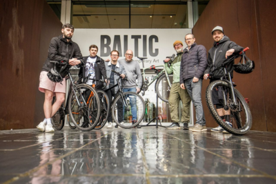 7 men stand outside Baltic entrance with bikes