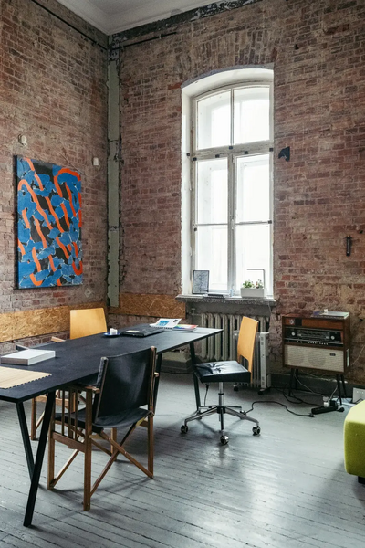 Brick walled room with wooden floors, a black table with chairs and colourful blue and orange painting displayed on the wall.