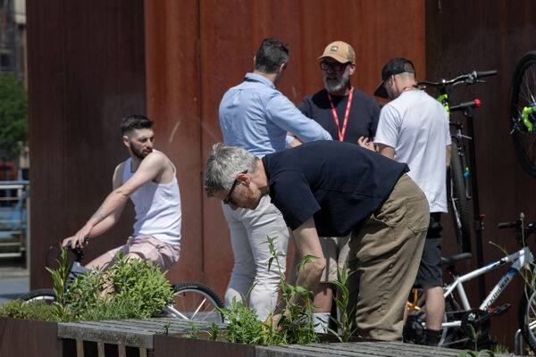People outside Baltic, some are talking, some are on bikes and one man is planting a plant in a planter