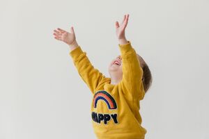 Child smiling with hands raised to the sky