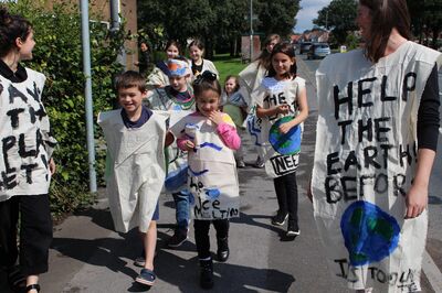 Children and adults walking along a pavement wearing tabards with Climate action statements