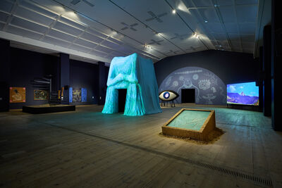 A large room full of sculptures, paintings and blue projections.
