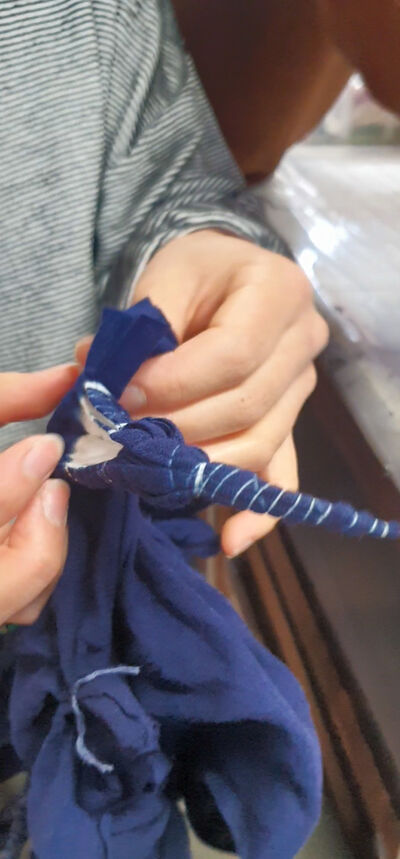 A person unravelling a tightly wound cloth to reveal a dyed pattern