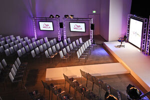 Large room with screens, metal seats facing a stage and purple lighting.