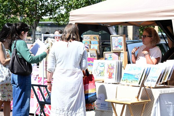 Two ladies looking at art 2D pieces from a seller.