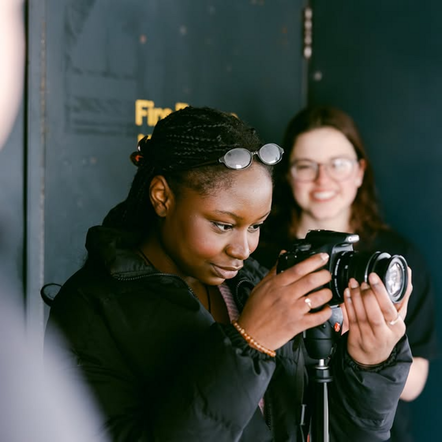 Young person smiling and looking through a camera lens.