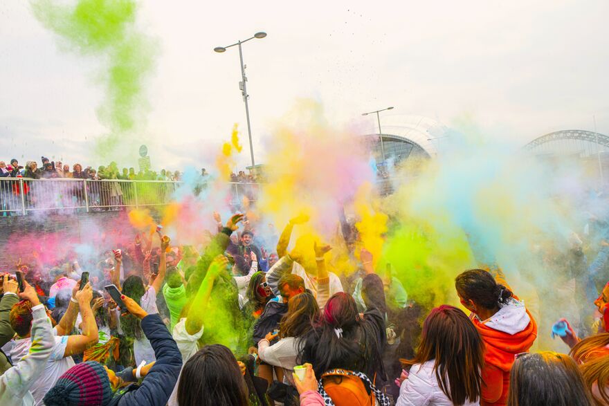 Crowd of people smiling with hands in the air throwing brightly coloured cloud paint.