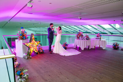 Couple stood in a suit and dress surrounded by colourful flowers and lights.