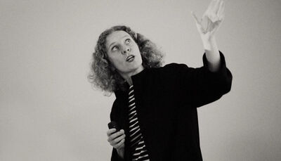 Black and white photo of a woman with curly hair, wearing a stripey top and black jacket looking upwards.