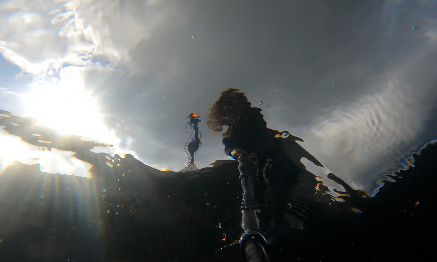 Silhouette of a person standing over water from the perspective of beneath the water surface.