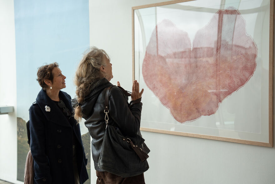 Two people stood infront of a framed print of the felled sycamore gap tree's rings, in the shape of a heart.