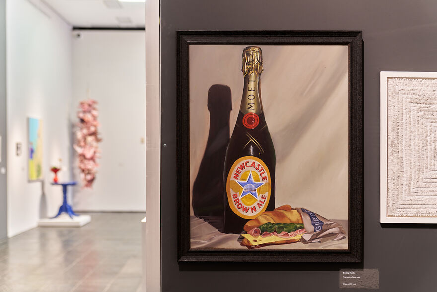 Framed painting of a bottle of newcastle brown ale with a Greggs cheese and ham baguette.