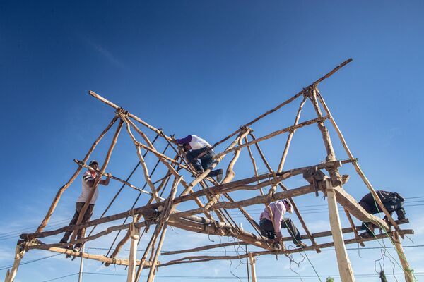 Wooden structure with four men climbing it against a blue sky.