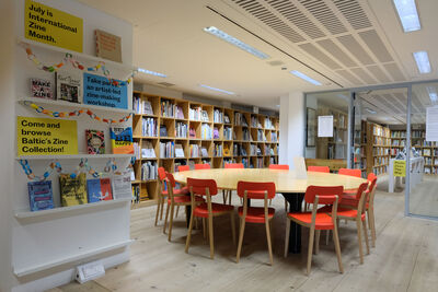 Room with bookshelves on the walls and a large circular table in the middle with red chairs.