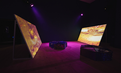 Two large screens propped up facing each other with orange and yellow coloured underwater landscapes projected on them in a dark blue and purple lit room.