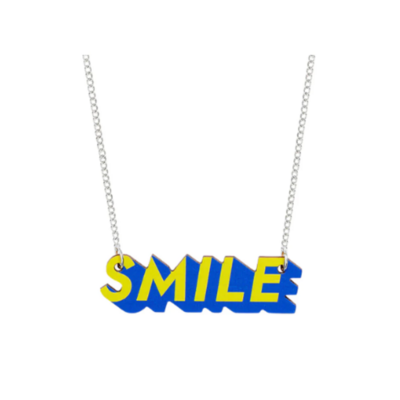 Silver necklace with large acrylic lettering in yellow and blue spelling out 'Smile'.