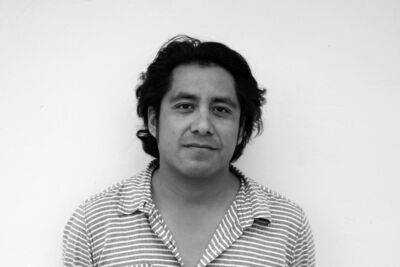 Man of colour with mid-length black hair wearing a stripy polo top.